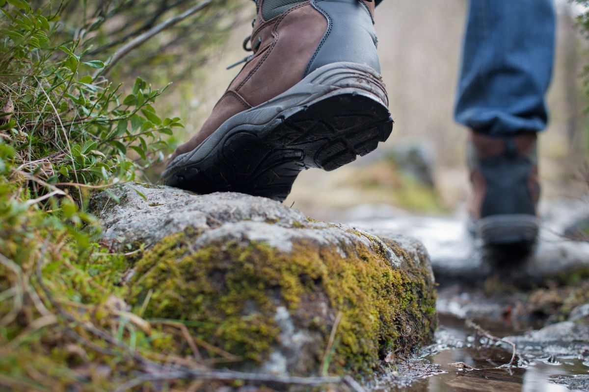 Walker wearing a pair of brown leather walking boots on a muddy path.