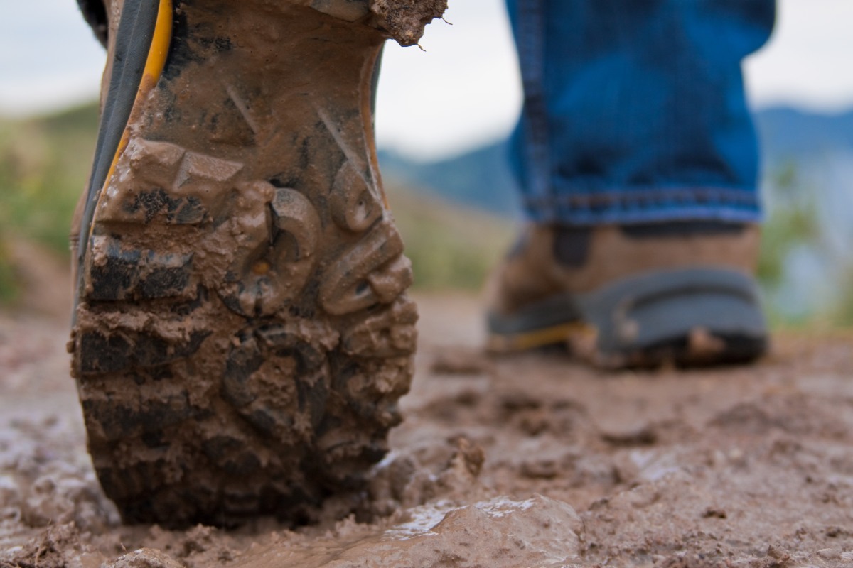 Close up of the sole on a pair of leather hiking boots as a walker walks along a trail.