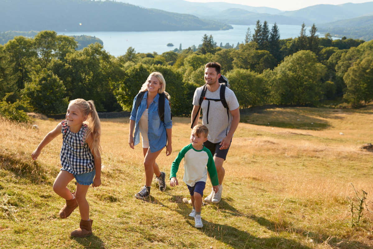 Young family enjoying a hard day walk in the summer sun in the Lake District enjoying the beautiful views through the forest to the lake below.
