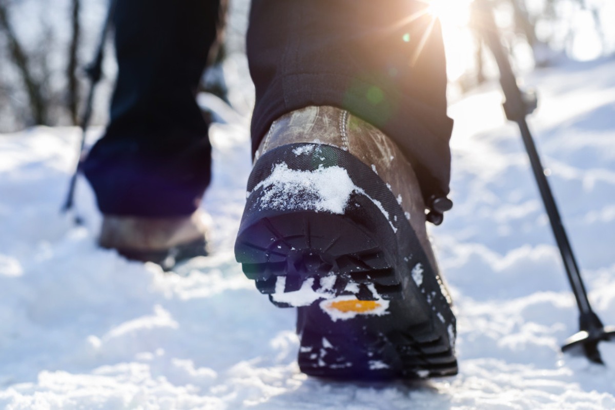 Walker walking in the snow in a pair of brown hiking boots using trekking poles.