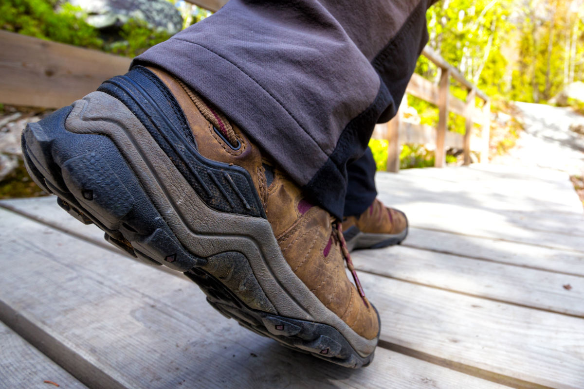 Walker wearing modern synthetic walking boots hiking along a trail leading into a forest.