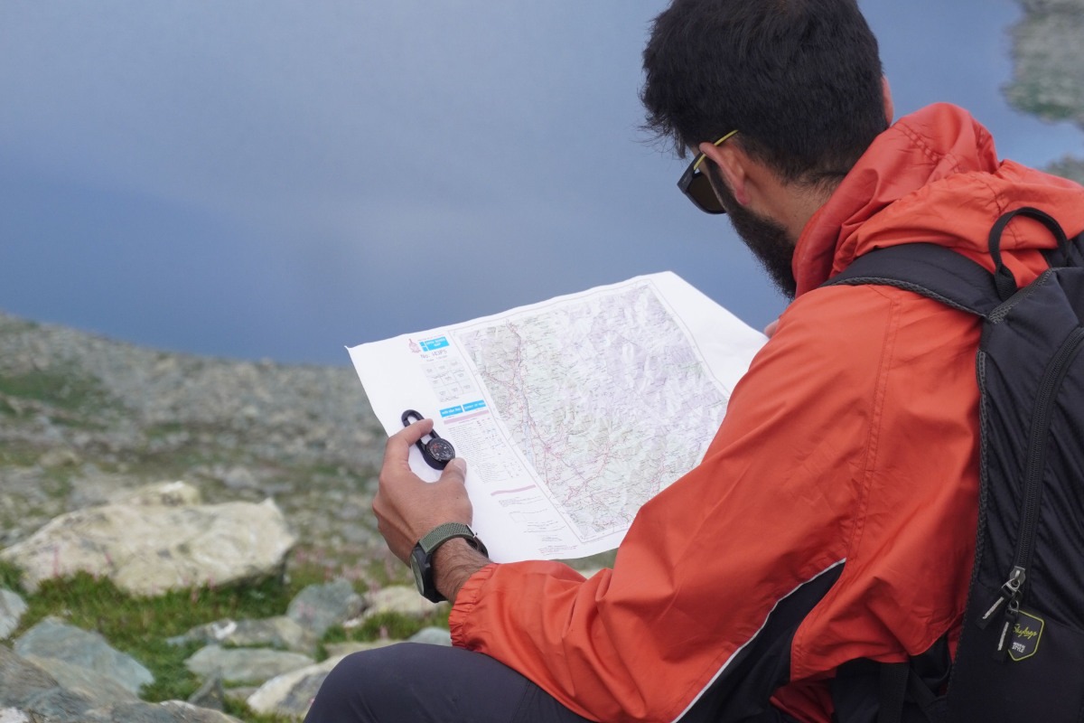 Man in a red waterproof jacket checking his map and compass for mountain safety.